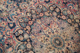 Vintage Persian Meshed carpet showing worn blush red, cobalt blue, and ivory floral motifs.