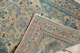 Folded corner of an antique Tabriz rug with intricate dusty teal, pale rose, ivory pattern and tattered fringe.