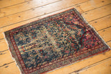 Upper corner of a Kerman rug featuring raspberry red border, indigo floral vines, and distinct abrash.