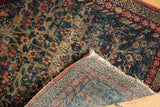 Hand-knotted Kerman rug corner revealing fine weave, tattered fringe, and tree-of-life pattern.
