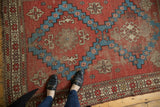 Antique Caucasian rug corner with geometric brick red, aqua, ivory patterns, subtle wear, and feet.
