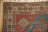 Antique Caucasian rug corner displaying a brick red field, aqua blue geometric motifs, and ivory patterned borders with mostly even wear.