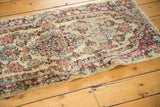 Vintage Kerman rug runner corner featuring rococo floral design, ivory, red, blue hues, and wear.