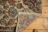 Folded corner of vintage Kerman rug reveals worn floral pile and hand-knotted reverse.