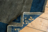 Curled antique Peking rug corner shows hand-knotted floral foundation and worn blue pile.