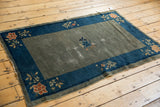 Antique Peking rug: muted green-gray field, deep cobalt blue border, simplified floral motifs, wear.