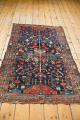 Tattered corner of a vintage Hamadan rug, revealing navy, red, and ivory rectilinear vinery patterns.