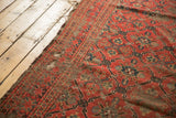 Antique Beshir carpet's tattered side, revealing wear, exposed foundation, and geometric design.