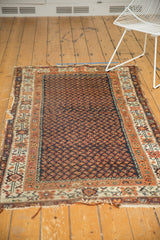 Tattered end of a vintage Hamadan rug, with geometric borders in ivory, orange, and red.