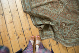 Partially unrolled vintage distressed Shiraz rug showcasing copper, sea foam, and terracotta floral patterns.