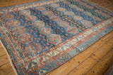 Corner of distressed Baktiari rug, showing worn pile, faded blue-red geometric patterns, and fringe.