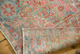 Distressed vintage Heriz rug corner, showcasing faded rectilinear patterns, fringed edge, and hand-knotted reverse.