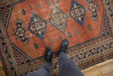 Vintage Persian Malayer rug with dusty rust blush field, navy geometric medallions, and evident wear.