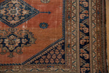 Vintage Malayer rug corner detail: dusty rust blush field, navy geometric motif, and multi-patterned borders showing wear.