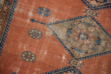 Dusty rust blush Malayer rug with navy blue geometric pattern, floral motifs, and visible wear.