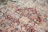 Aged pile of antique Kerman rug, showing faded cochineal, ivory floral arabesques, and visible knot heads.