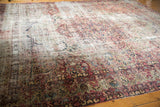 Detail of a classic floral antique Kerman carpet, displaying faded cochineal red and navy blue motifs, with visible wear.