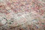 Antique Kerman carpet with visible threadbare floral patterns and scattered knot heads.