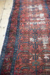 Dark dusty rose Persian Lilihan runner with blue border, germinating plant motifs, and visible wear.