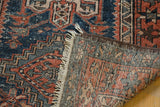 Hand-knotted vintage Karaja rug's folded corner shows geometric navy, rust, ivory patterns and fringe.