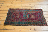 Vintage Lilihan rug corner with dark raspberry red field, blue florals, and tattered fringe.