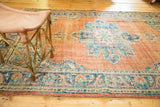 Scalloped medallion detail of distressed vintage Oushak carpet in faded tangerine and blue.