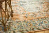 Textured distressed field of a vintage Oushak rug with tangerine and blue floral motifs.