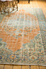 Distressed Oushak carpet detail: dusty tangerine field with visible wear, blue vinery border.