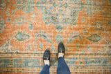 Distressed Oushak rug showing a person's feet, worn rusty orange pile, and blue floral motifs.