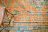 Distressed vintage Oushak rug with worn orange field and blue border, featuring floral motifs.