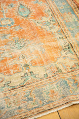 Distressed Oushak rug corner with rusty orange and sky blue floral pattern, worn pile, and fringe.