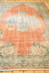 Vintage Oushak rug's distressed tangerine orange pile, blue rococo details, and visible wear.