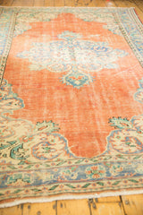 Distressed Oushak corner: tangerine orange, dusty blue Rococo motifs, mostly even wear.