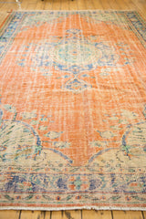 Distressed Oushak rug border: burnt orange, royal blue, ivory floral motifs, and fringe.