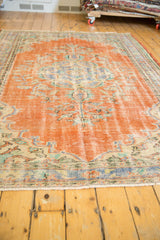 Vintage Oushak rug showing decorative wear in vibrant orange, blue, and sand tones.
