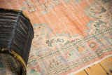 Distressed Oushak carpet close-up with faded peach pile, Rococo border, and visible foundation.