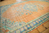 Distressed vintage Oushak rug with faded tangerine field, visible foundation, and blue floral border.