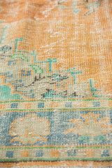 Distressed vintage Oushak pile with faded tangerine, blue, and mint geometric motifs.