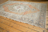 Distressed Oushak rug corner showing faded apricot field and charcoal vine border.