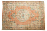 Distressed vintage Oushak carpet with a central scalloped medallion, dusty rose field, and pastel vine borders, 7x10.