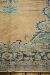 Distressed Oushak carpet texture with pale apricot field, visible wear, navy and mint green motifs.