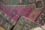 Distressed magenta and green pattern on a vintage Oushak rug, showing its hand-knotted foundation.