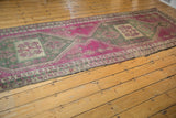 Geometric border and abrashed fuchsia and sage field of a distressed Oushak runner.