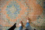 Distressed Oushak carpet's apricot peach, mint, and blue floral patterns underfoot.