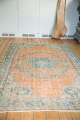 Distressed Oushak rug corner, showing faded apricot peach and mint green floral motifs.