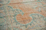 Textured surface of vintage distressed Oushak rug with faded ivory, orange, and blue scrolling patterns.