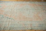 Distressed Oushak rug texture showing pale tangerine orange, mint green, and visible foundation.