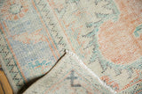 Distressed Oushak rug's textured pile with ivory, tangerine, blue hues and visible fringe.