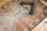 Distressed Oushak rug close-up: terra cotta, ivory pile, geometric medallion, visible foundation.