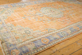 Distressed Turkish Oushak carpet, showing even wear, faded tangerine orange, royal blue, and ivory tones.